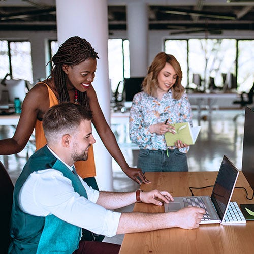 Three colleagues collaborating around a laptop, discussing work in a modern office.