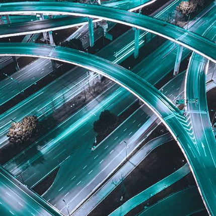 Aerial view of a multi-level highway interchange at night with teal light trails from moving traffic.