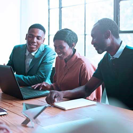 Three colleagues sitting at a table, collaborating and looking at a laptop