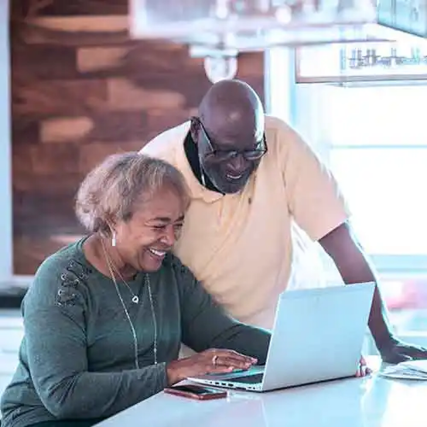 Older couple smiling while using a laptop together at a kitchen counter in a modern home.