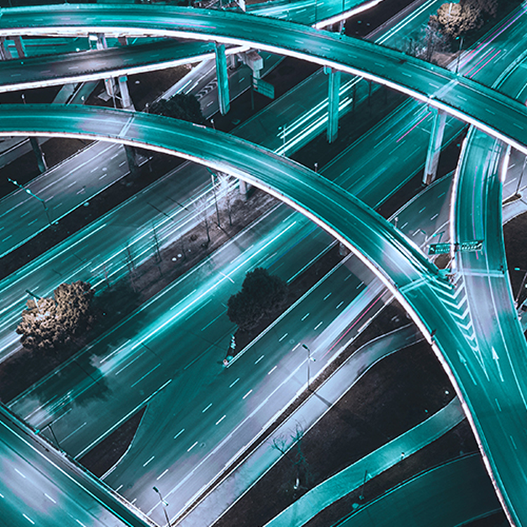 Aerial view of a multi-level highway interchange at night with teal light trails from moving traffic.