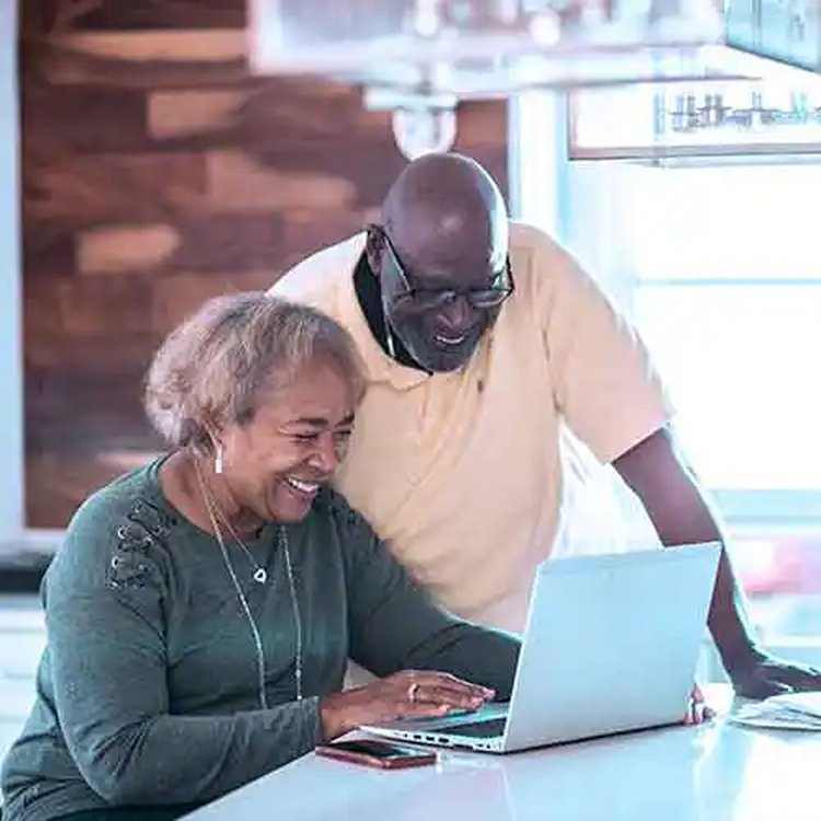 Older couple smiling while using a laptop together at home